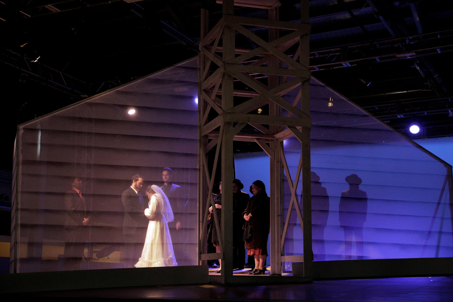 Behind a translucent frame shaped like a house, a man and a woman are exchanging wedding vows.